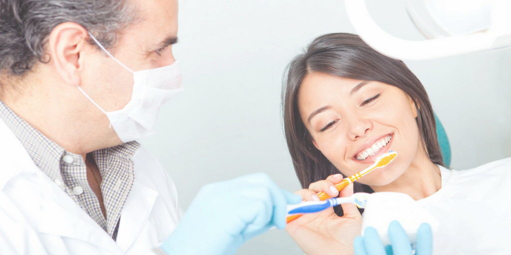 Mask-wearing dentist offering two toothbrushes to patient