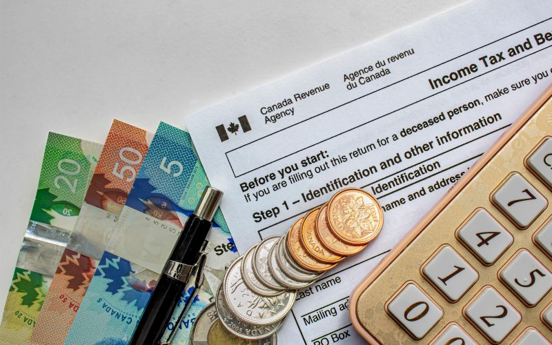 Calgary, Alberta, Canada. July 20, 2020. Canadian Tax Forms with coins, calculator, a pen and bills on a white table. Tax time concept